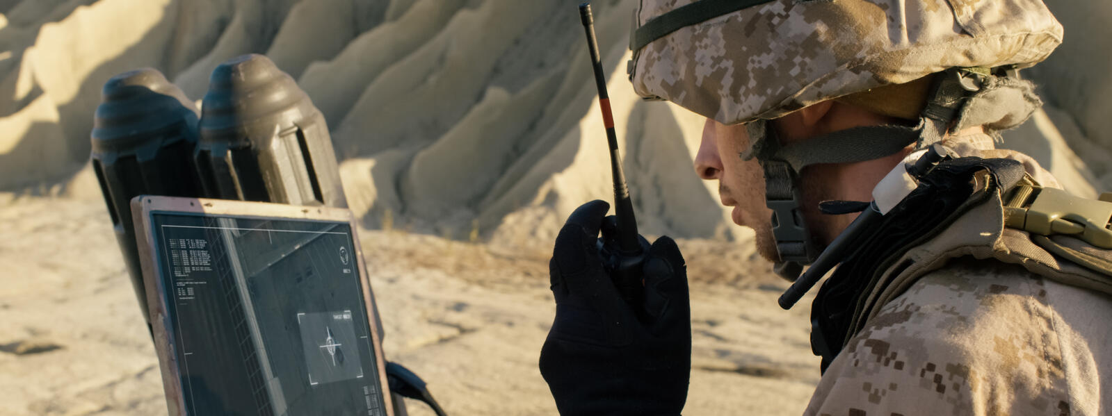 Military soldier viewing video feed on laptop monitor.